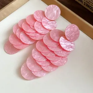 Close-up of pink marbled acrylic round disc tassel earrings for a vacation look.