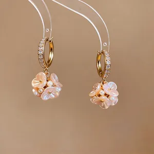 Macro vista di eleganti orecchini a cerchio in oro con zirconi e fiori di madreperla.