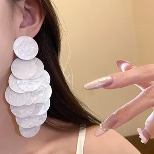 Close-up detail of white acrylic marbled circular tassel earrings worn by a model