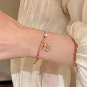 Detail view showing a hand-woven pink cord bracelet with cherry blossom and pearl charm