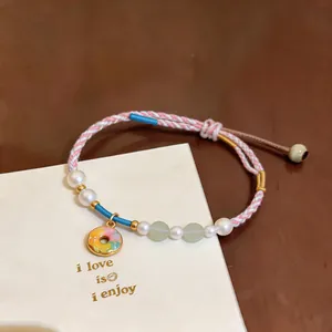 Detailed view of handwoven pearl bracelet with colorful donut charm on cream card