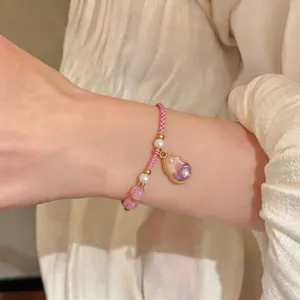 Detailed view of a hand-woven pink rope bracelet with pearls and a gourd charm on a wrist