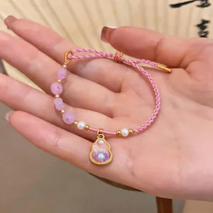 Close-up of a pink braided bracelet with pearls and a gold gourd pendant on a palm