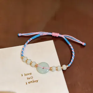 Detail view of a hand-woven pink and blue cord bracelet with light green jade-like beads