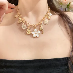 Détail d'un collier doré avec pendentifs coquillages et fleurs porté au cou.