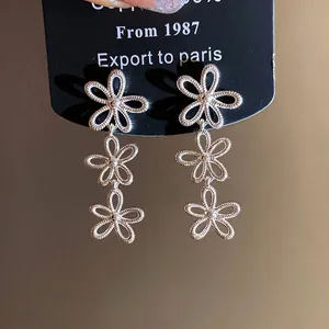 Elegante silberfarbene Ohrhänger mit hohlen Blumen auf schwarzer Karte, minimalistisch.