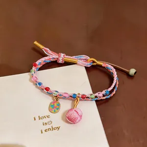Close-up of hand-woven colorful rope bracelet with beads and pink charm on white card