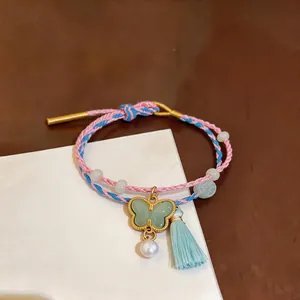 Close-up of handmade woven bracelet featuring a jade butterfly pendant, pearl, and tassel