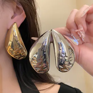 Detailed macro view of large metallic water drop earrings in gold and silver finish.
