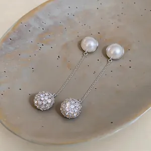 Detailed close-up of elegant pearl and crystal ball dangle earrings on a ceramic plate.