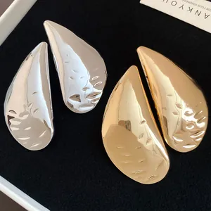 Detail view of oversized teardrop stud earrings in gold and silver metallic finishes.