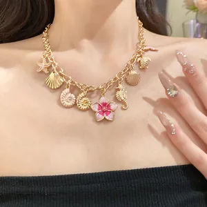Gros plan d'un collier en chaîne dorée avec des breloques océan et une fleur rose