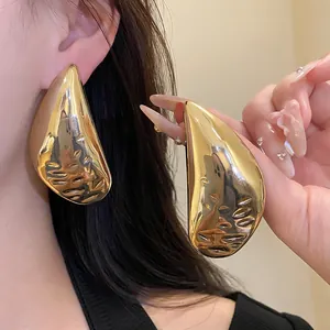 Close-up of oversized gold teardrop earrings with hammered texture detail