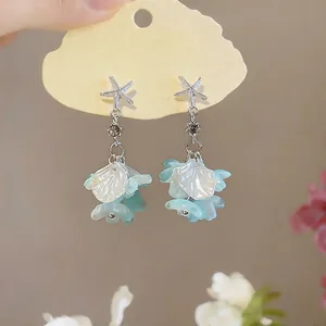 Détail de boucles d'oreilles étoile de mer et fleurs aux pétales bleus clairs