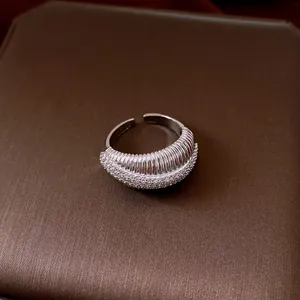 Vista dettagliata di un anello aperto argento con texture a costine e brillanti zirconi.