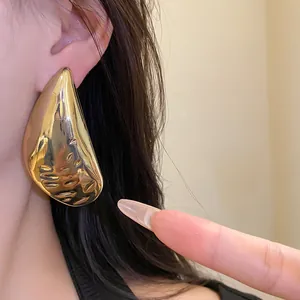 Close-up of large gold teardrop stud earring with hammered metal texture
