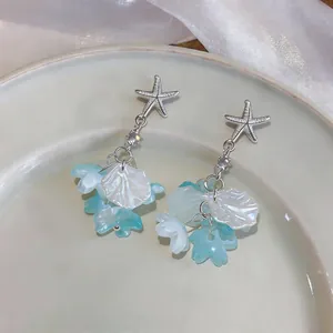 Détail de boucles d'oreilles étoile de mer avec glands en coquille et pétales bleus