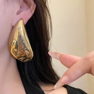 Detailed view of a large gold water-drop earring with hammered texture on a model