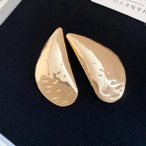 Detailed close-up of textured gold teardrop stud earrings on a dark velvet surface