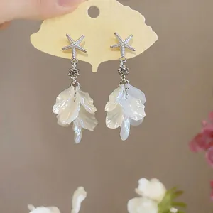 Gros plan de boucles d'oreilles étoile de mer avec strass et pétales blancs