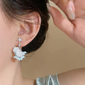 Détail de boucles d'oreilles étoile de mer avec glands de fleurs en coquillage