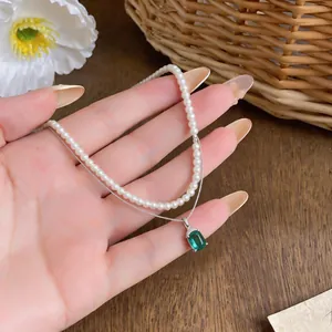 Dettaglio ravvicinato di una collana di perle a doppio strato con pendente in zircone verde.