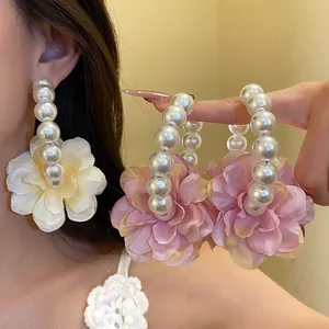 Gros plan de grandes créoles en perles avec pétales de fleurs en tissu et aiguilles en argent