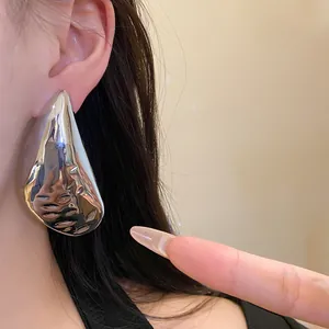 Close-up of large silver teardrop stud earrings showing metallic texture and high shine