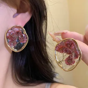 Exquisite detail view of gold-rimmed resin stud earrings with delicate dried pink flowers.