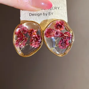 Close-up of gold-toned resin stud earrings featuring real dried pink flowers inside.
