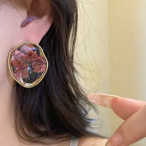 Close-up view of delicate resin flower stud earrings with a gold frame on a woman's ear