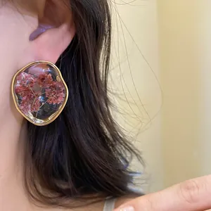 Close-up detail of resin stud earrings with real dried flowers and a gold edge
