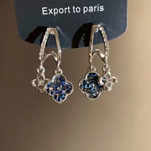 Elegant silver needle clover earrings with blue rhinestones presented on a black card