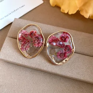 Close-up of irregular gold-tone stud earrings with dried pink flowers in clear resin