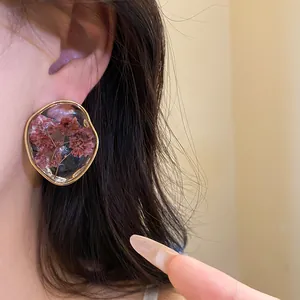 Close-up detail of resin stud earrings featuring real dried flowers in gold frame