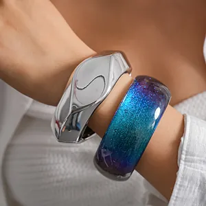 Close-up detail of a silver fluid metal bangle and a blue glitter resin bracelet on a wrist