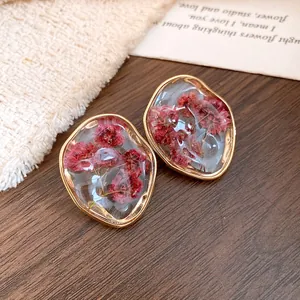Detailed close-up of dried red flowers preserved in irregular resin earrings with gold trim.