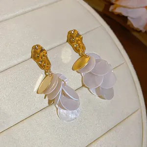 Close-up of gold dangle earrings with cascading translucent shell discs.