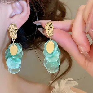 Close-up detail of elegant gold and mint green shell tassel earrings worn by a model