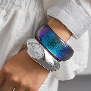 Macro view of chunky metallic silver and glitter resin gradient bangles on a wrist.