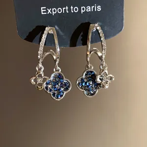 Close-up of elegant silver needle earrings with blue rhinestone flower pendants