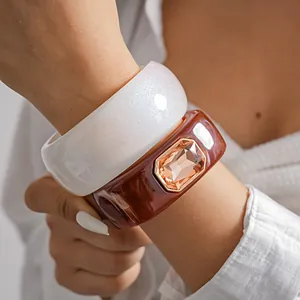 Detail view of chunky white pearlescent and amber resin bangles with a large rhinestone.
