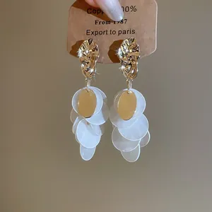 Macro detail of gold hammered earrings featuring cascading white shell disc tassels