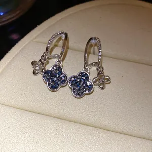 Detailed view of silver flower stud earrings with blue crystals on beige jewelry box