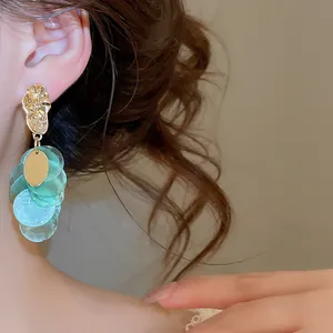Detail view of elegant shell tassel earrings with light green discs and gold metal.