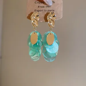 Close-up of elegant teal shell tassel earrings with textured gold accents for resort style.