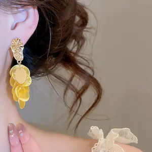 Detailed macro view of yellow shell tassel earrings with gold irregular textured studs.