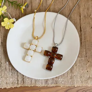 Simple fashion resin cross pendant necklaces in white and amber on a white display plate.