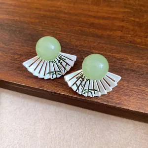 Detailed macro view of fan-shaped resin stud earrings with green beads and bamboo pattern.