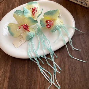 Close-up of floral fabric hair clip with light blue bead tassels on a white plate.